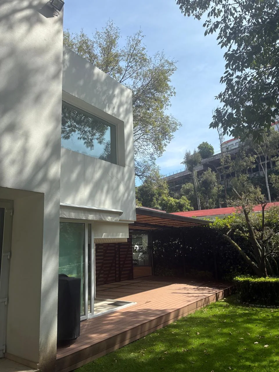 Exterior residencial blanco con terraza de madera y jardín arbolado