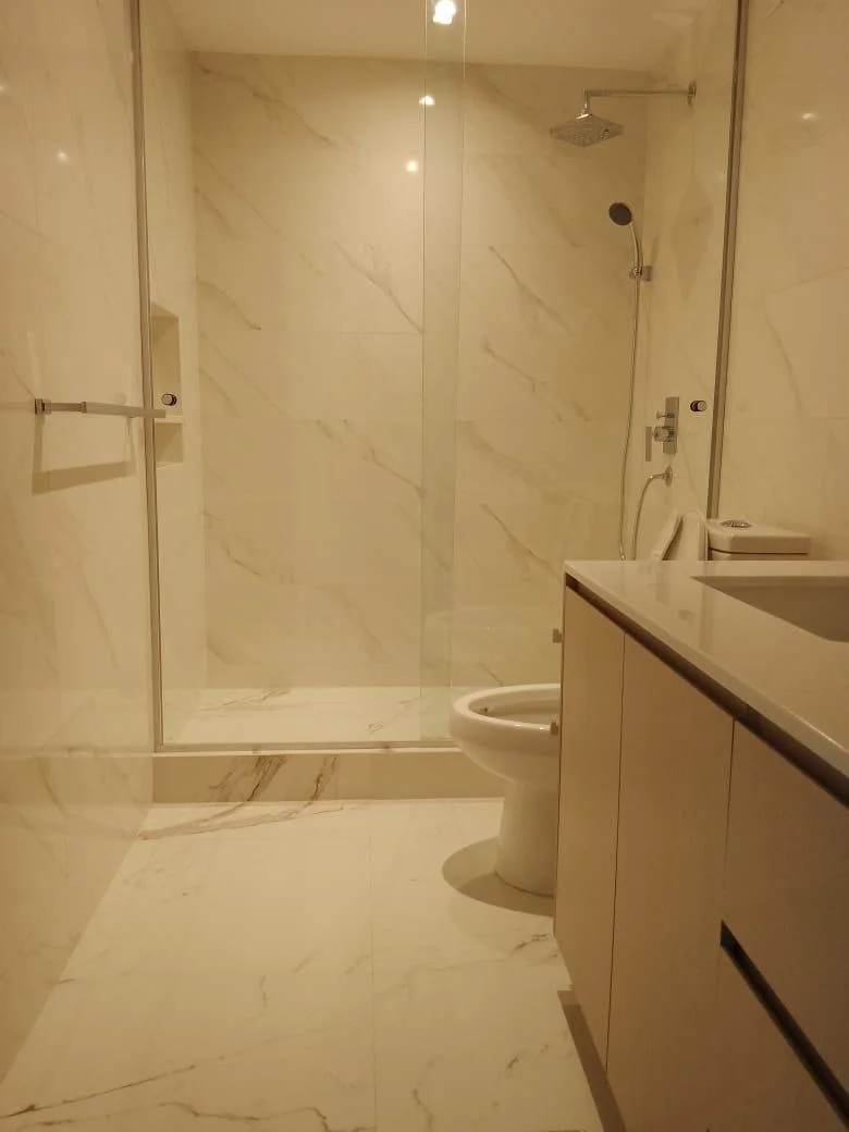 Baño remodelado con ducha de vidrio y acabados de mármol claro